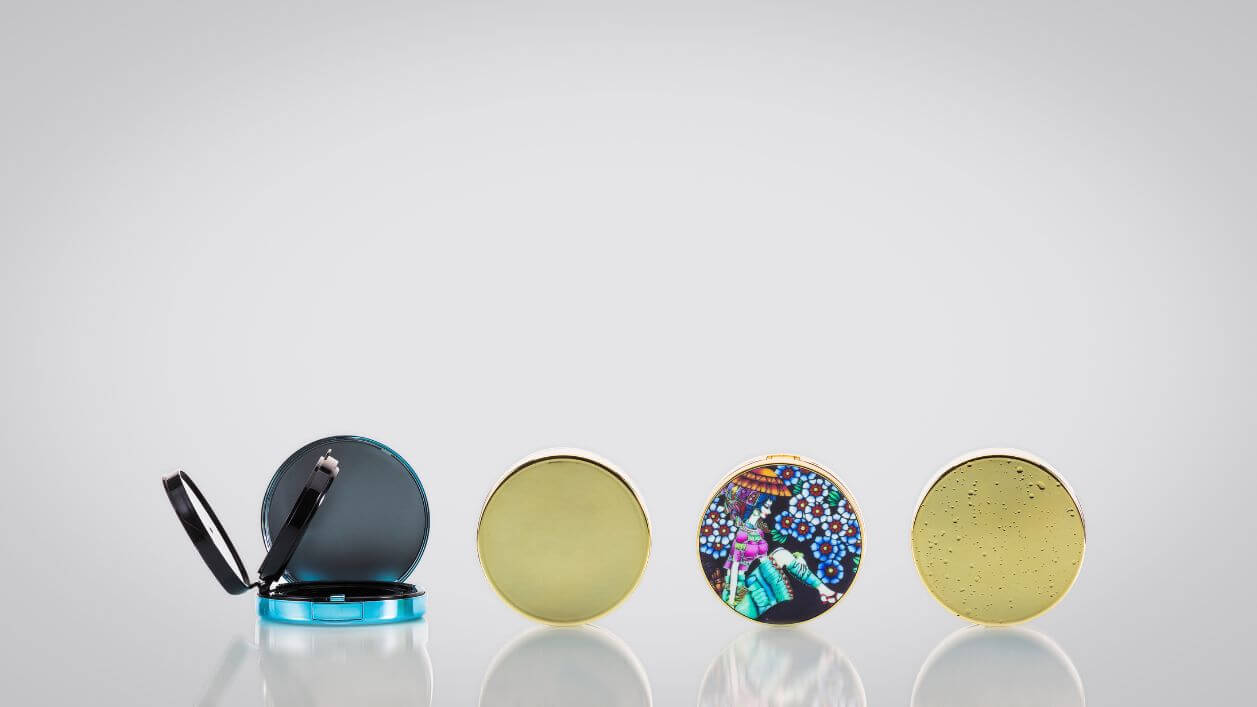 Printed cosmetic compacts featuring custom branding and decorative designs.