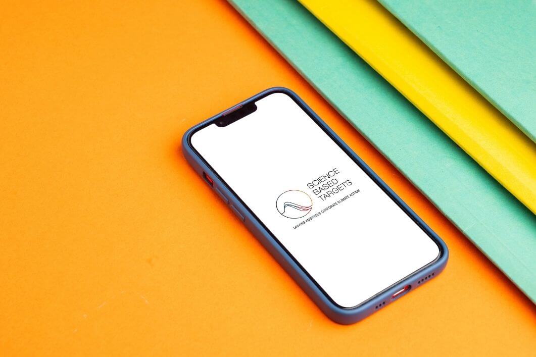 Science-Based-Targets-On-Phone Science based targets logo on phone, with an orange and teal background.