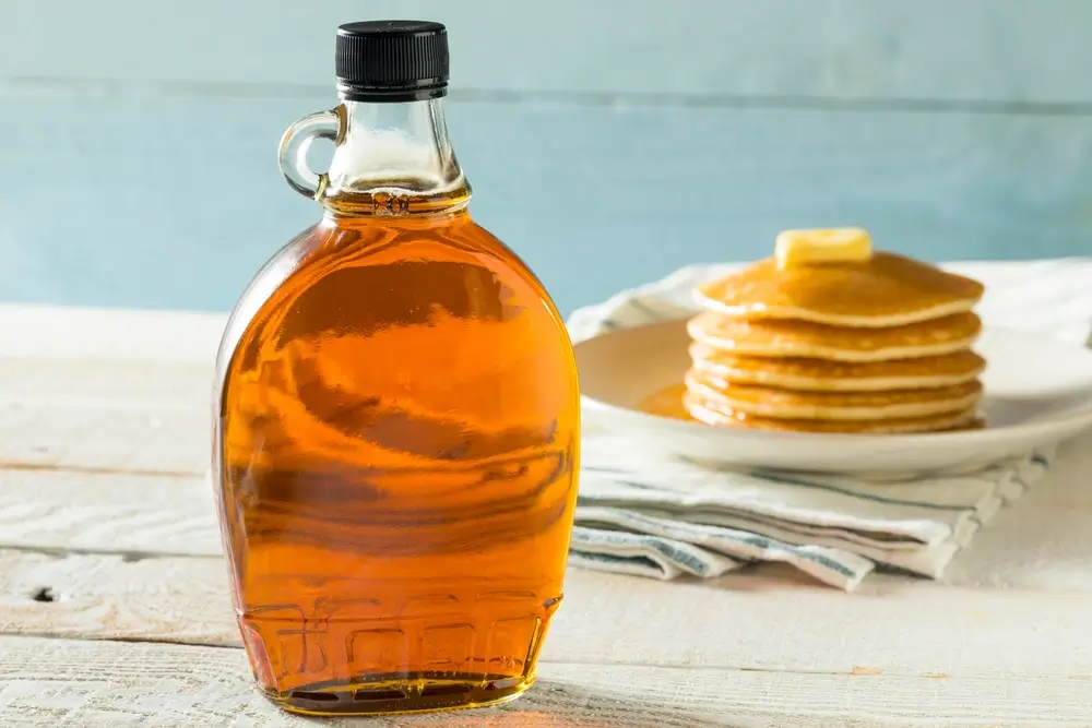 Filled maple syrup bottle, with pancakes in the background.