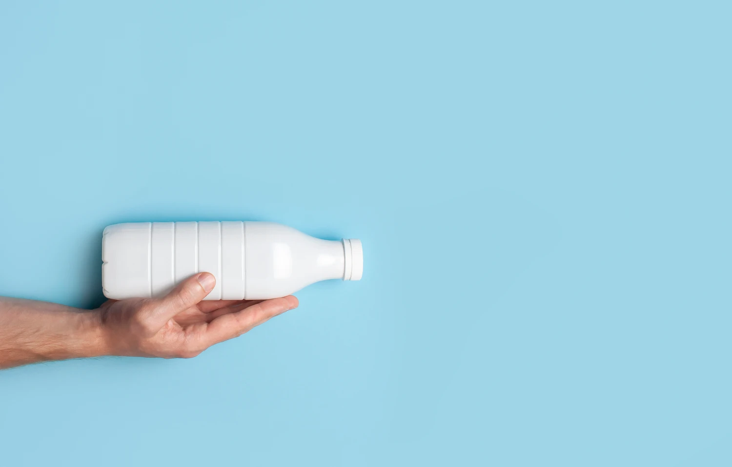 Plastic beverage bottle being held in front of blue background.