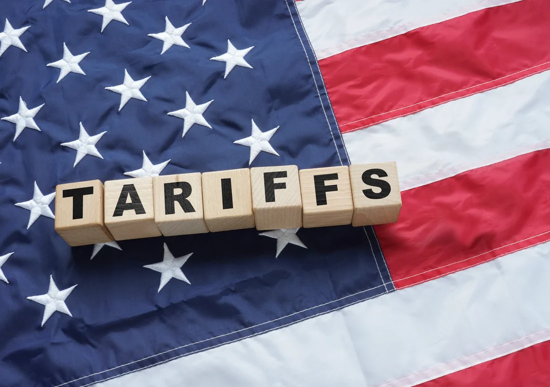 US flag as background with tariffs spelled out in blocks.
