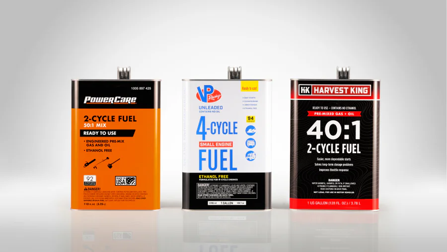 Rectangular metal gallon cans for premixed engine fuel with printed orange, white-blue, and black-red labels, flat metal tops, and threaded pour spouts.