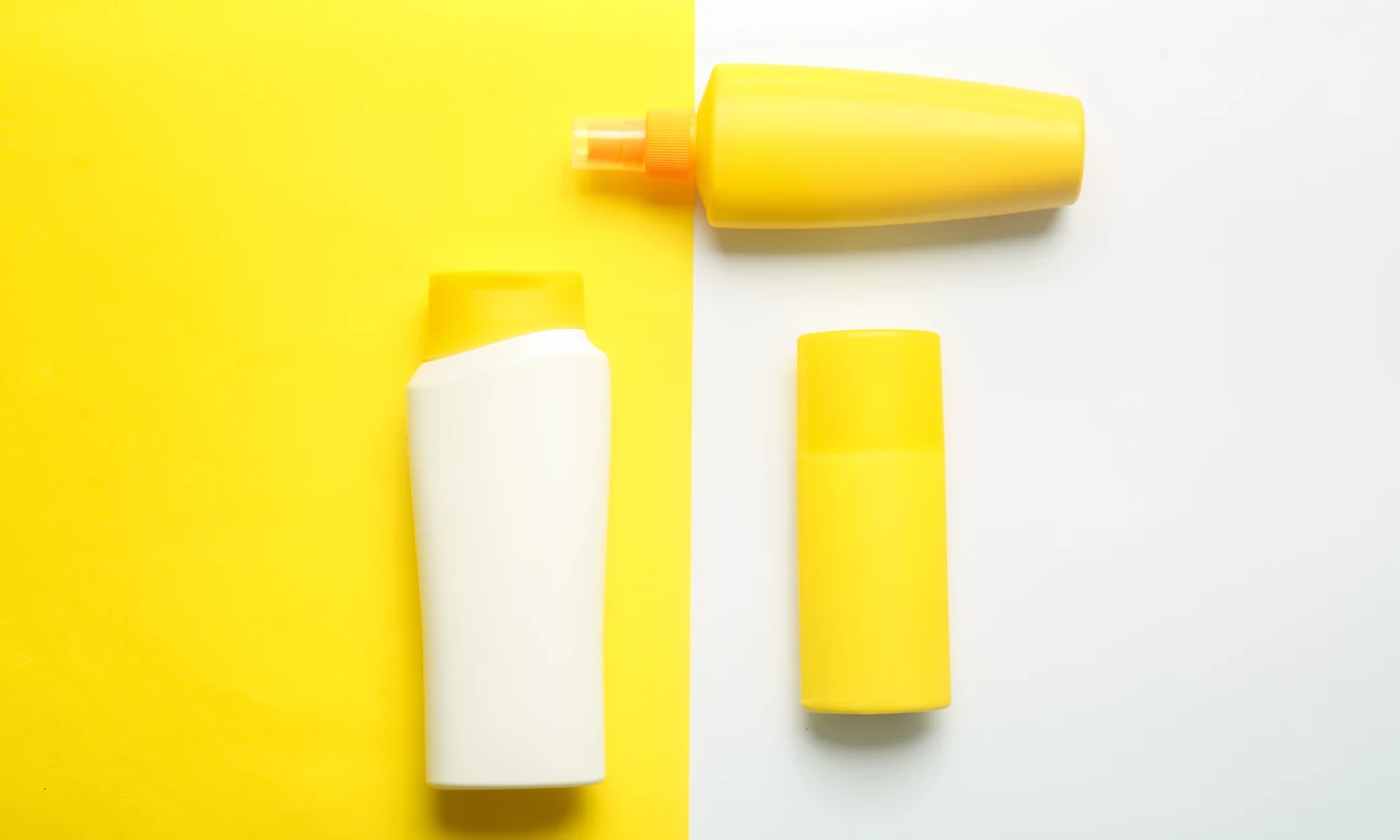 Yellow and white sunscreen packaging with a spray bottle, squeeze bottle, and solid stick container on a split background.